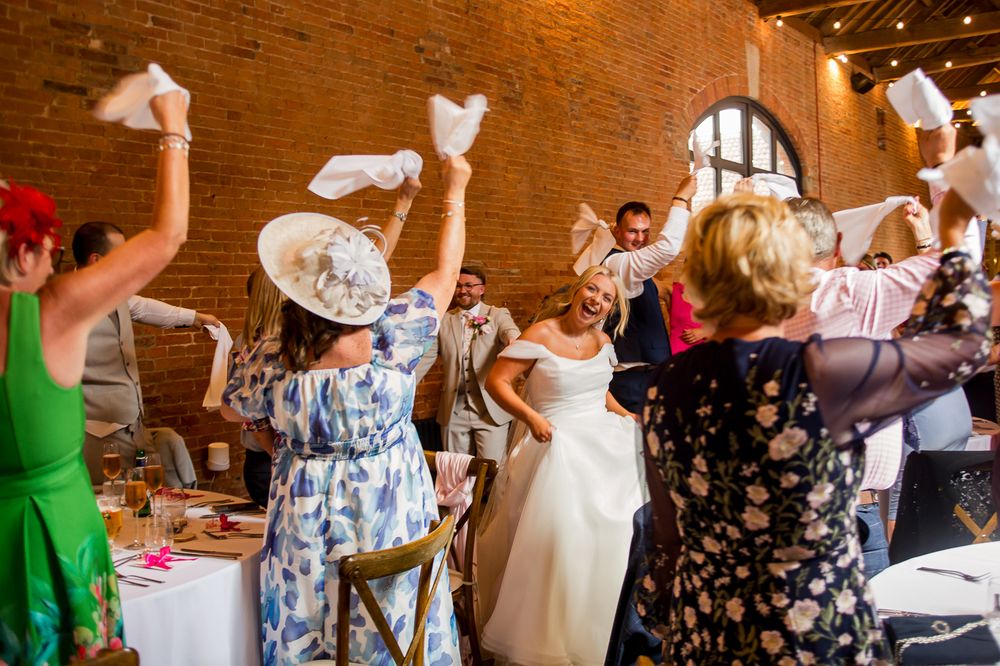 Wedding celebration with guests waving white napkins in unison at rustic indoor venue.