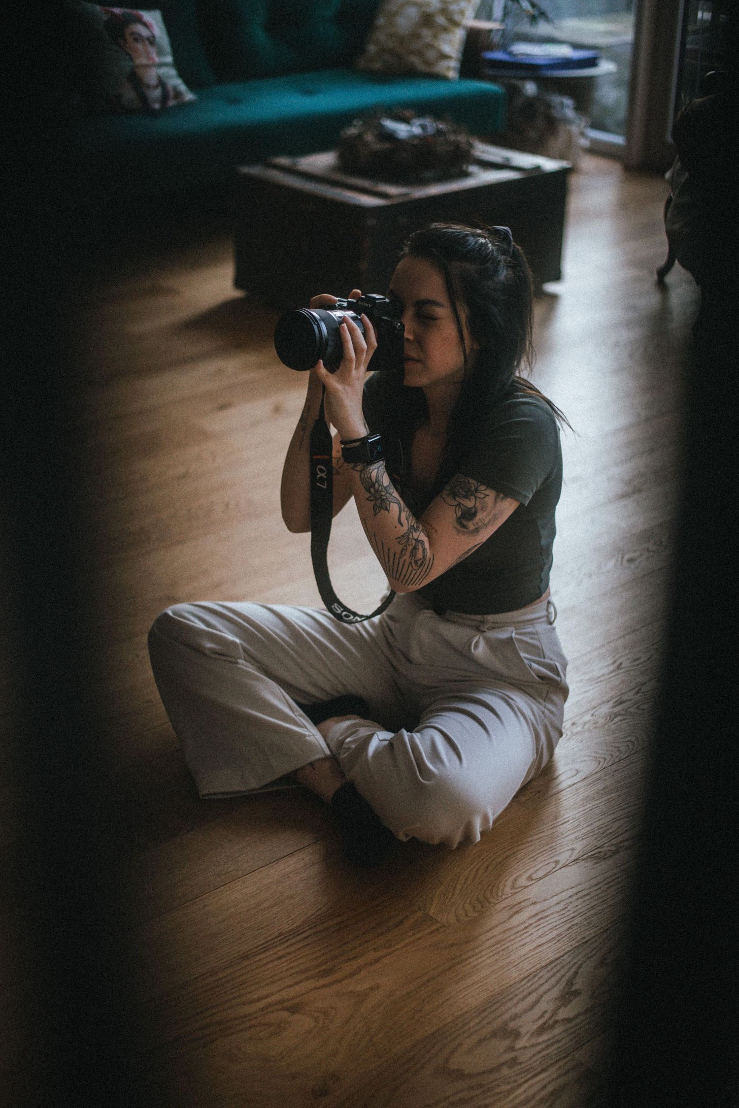 Photographer sitting cross-legged on wooden floor taking photos in dim lighting.