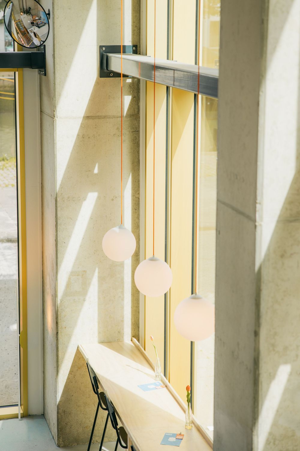 Minimalist pendant globe lights hanging by a sunny window with concrete walls and a narrow desk below.