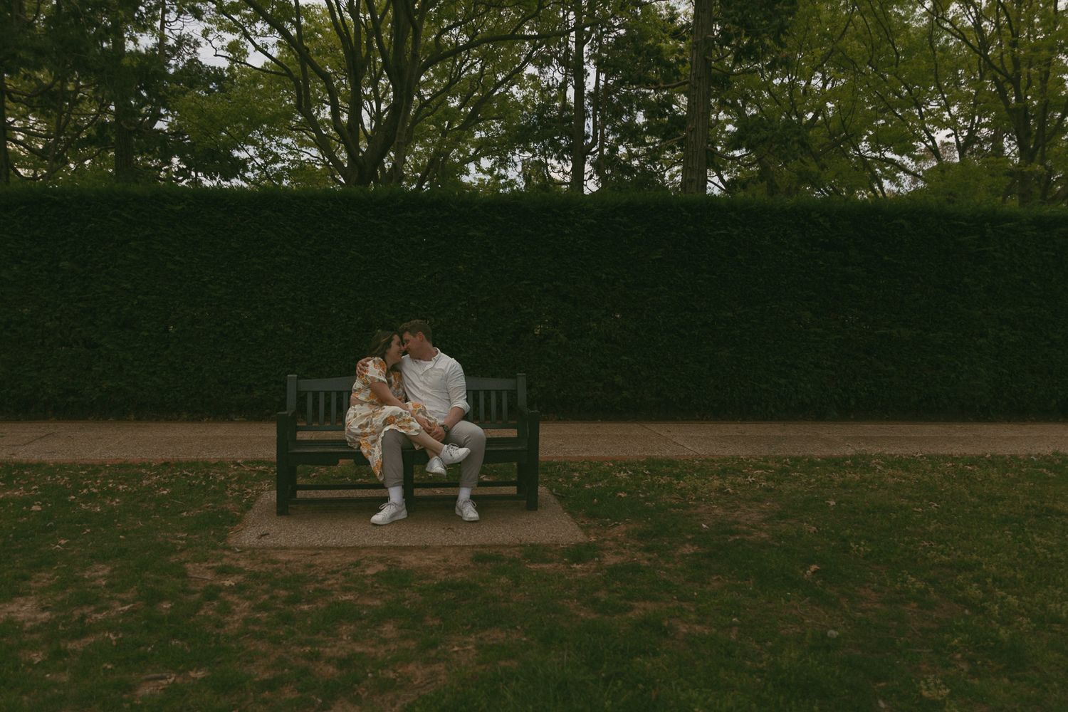 A couple sitting on a park bench with their foreheads together in a cinematic way.