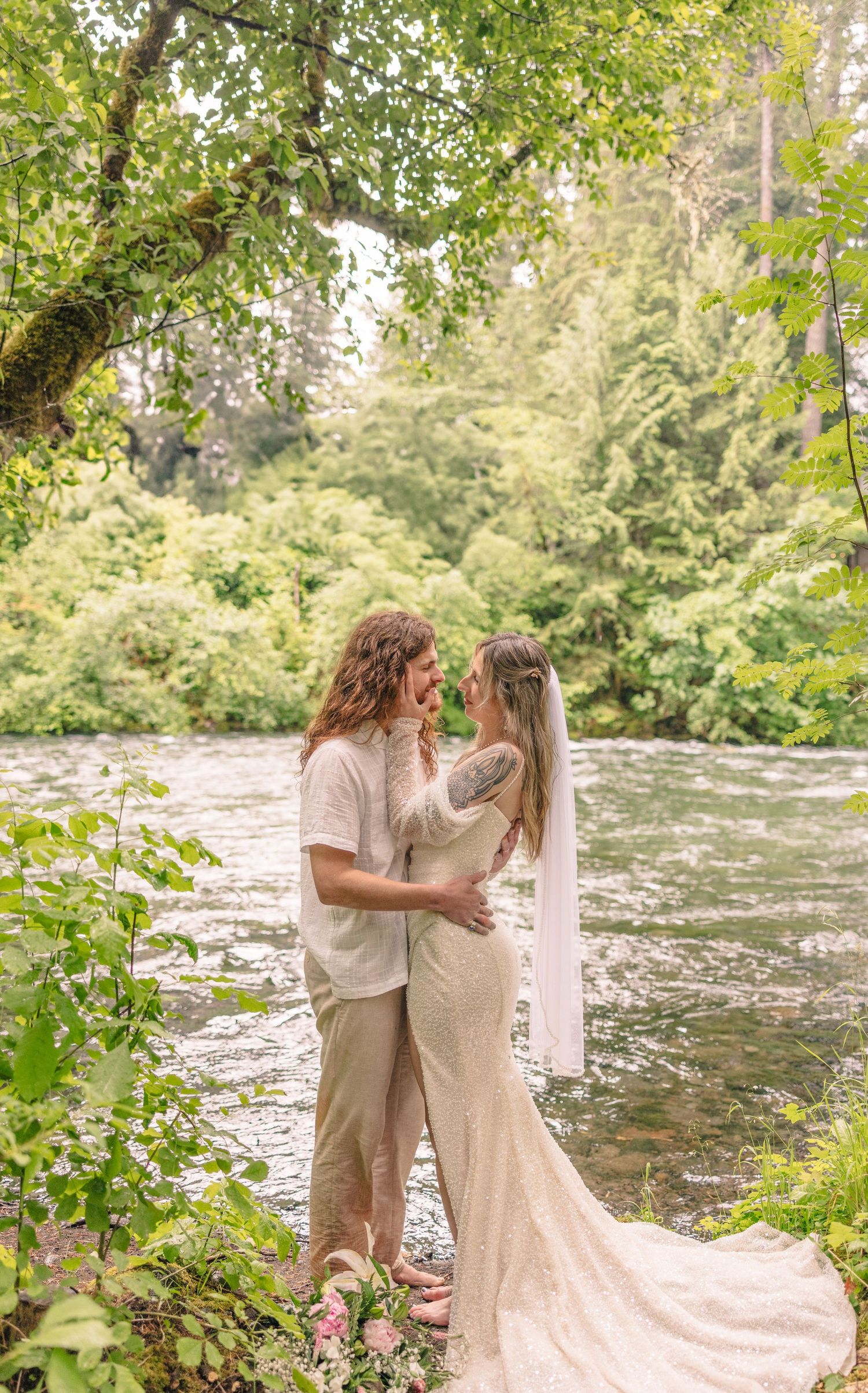 Couple in light colored attire sharing an intimate moment by a rushing river.