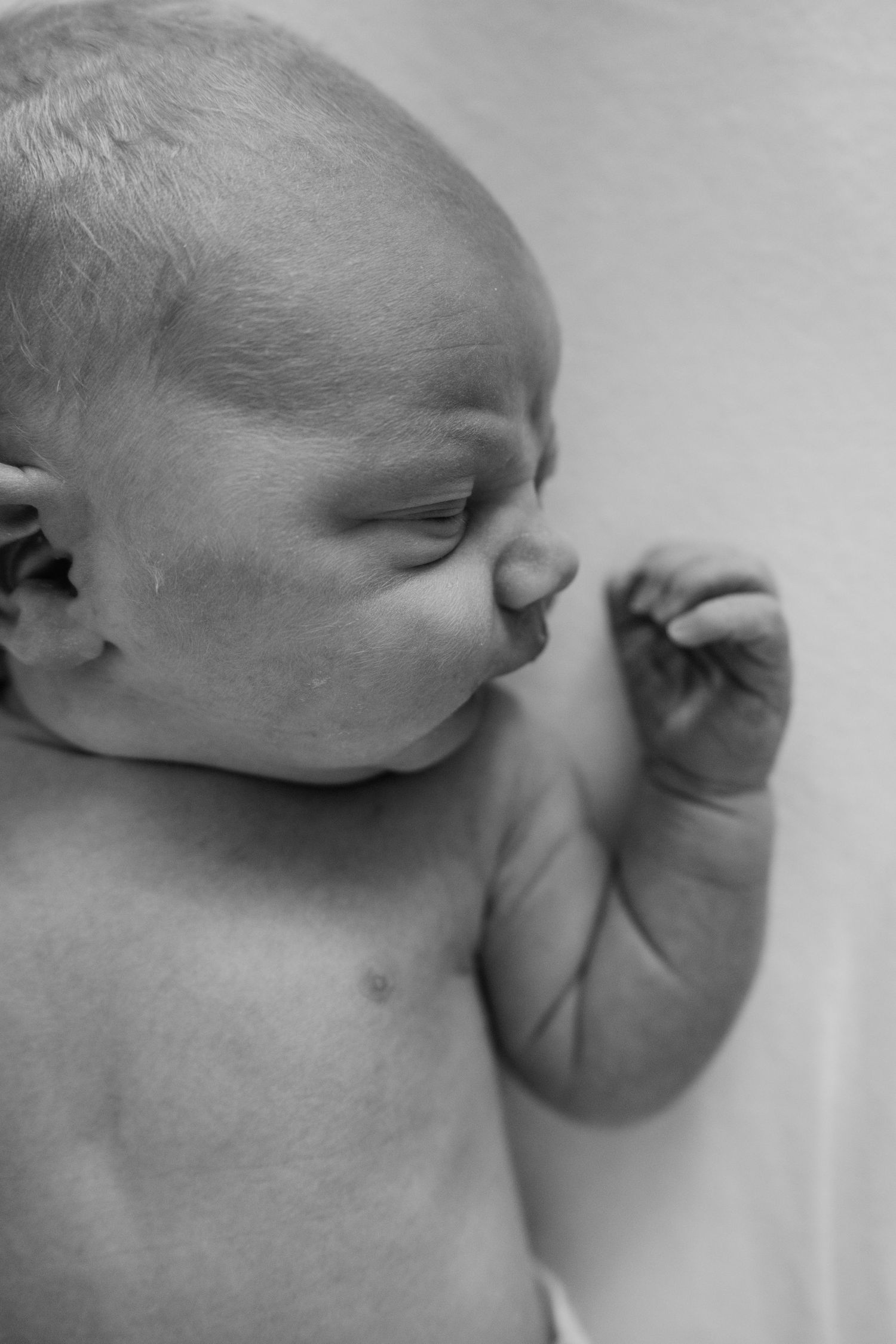 Black and white close-up portrait of a newborn baby lying on a white surface.