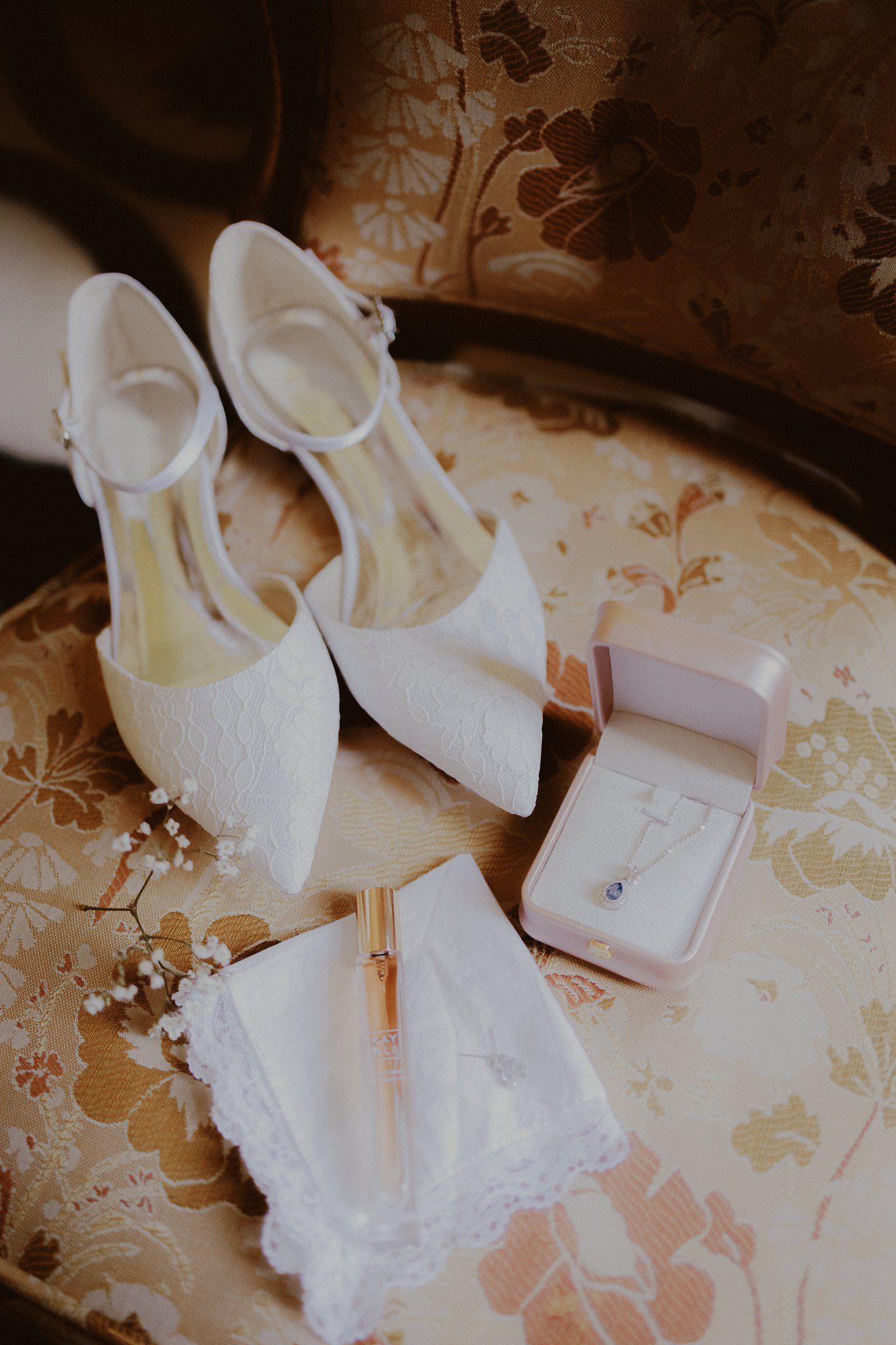 Close-up of delicate white ballet shoes and ribbons arranged on a vintage floral patterned surface.