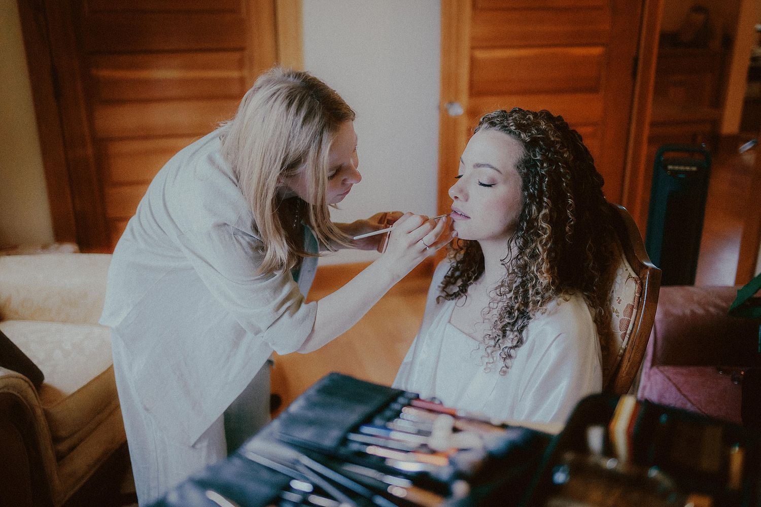 A makeup artist applies cosmetics during a wedding preparation session in a warmly lit room.