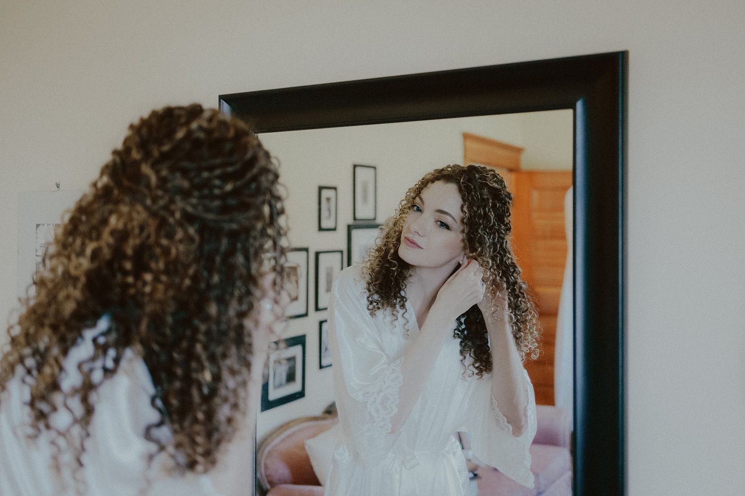 A mirror reflection captures someone in a white lace wedding dress with curly hair.