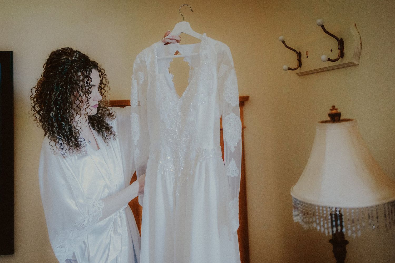 An elegant white wedding dress hanging on display next to antique decor.