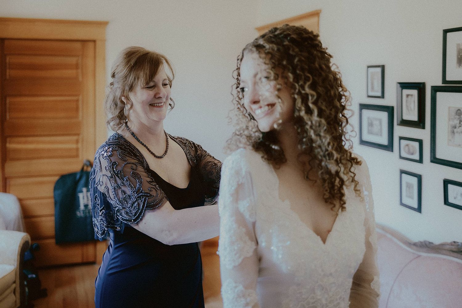 A touching moment during wedding preparations in a room with framed photos on the wall.