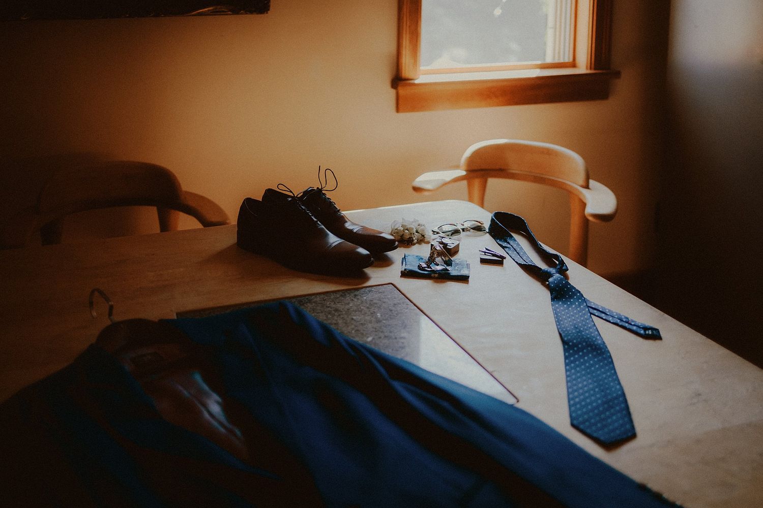 A blue suit jacket, tie and dress shoes laid out on a table in preparation.