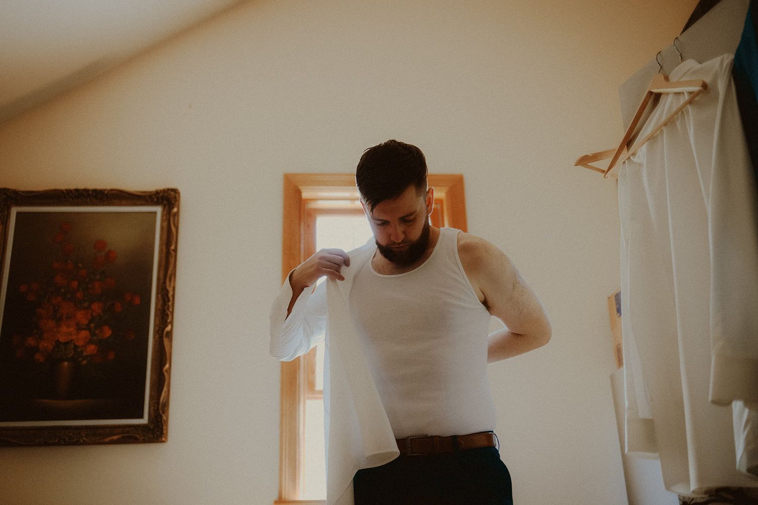 A person adjusts their outfit while getting dressed in a room with wooden window frames.
