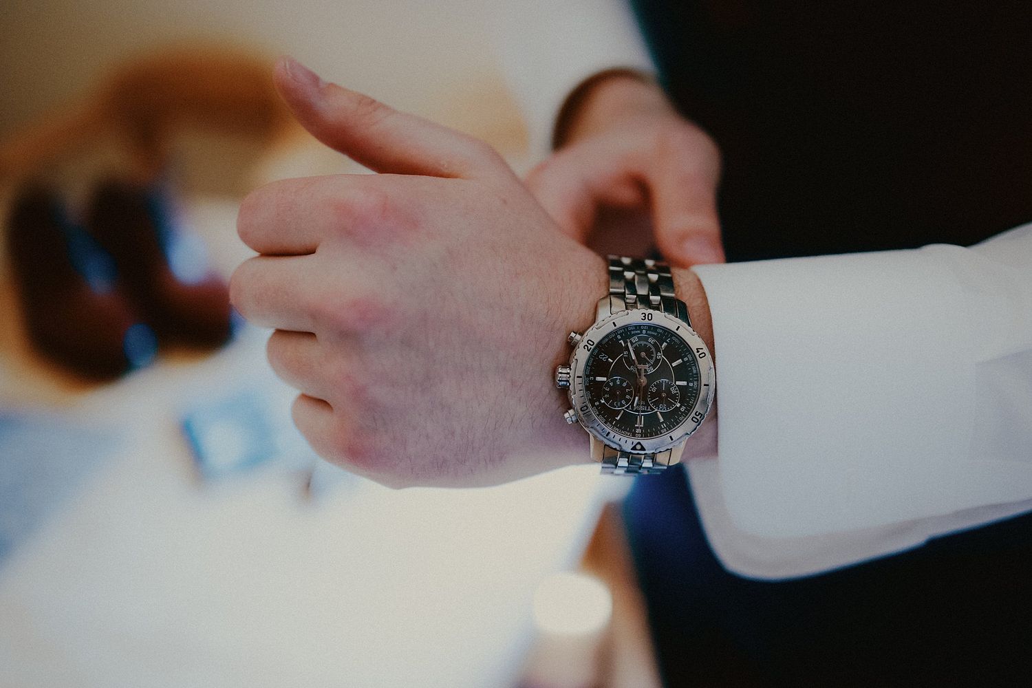 Close-up of a silver watch on a formal dress shirt sleeve.