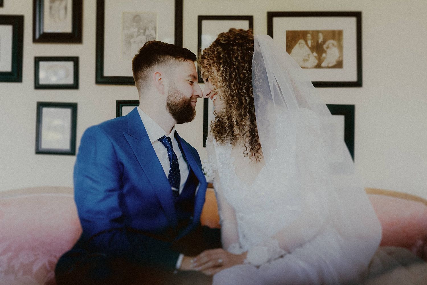 A romantic first look moment between newlyweds against a wall of framed artwork.