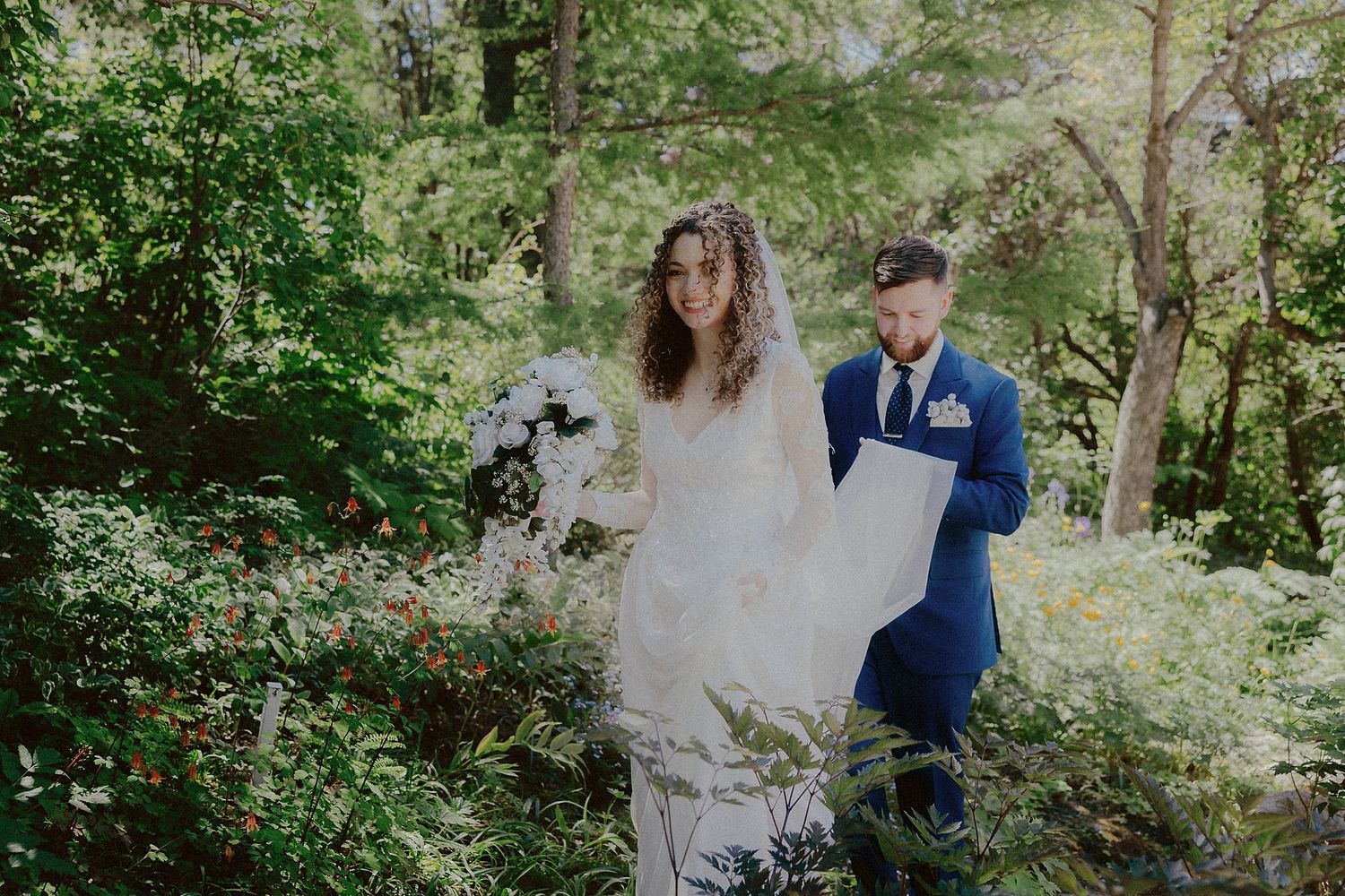 Couple walking together on a lush green forest path during an outdoor photo session.