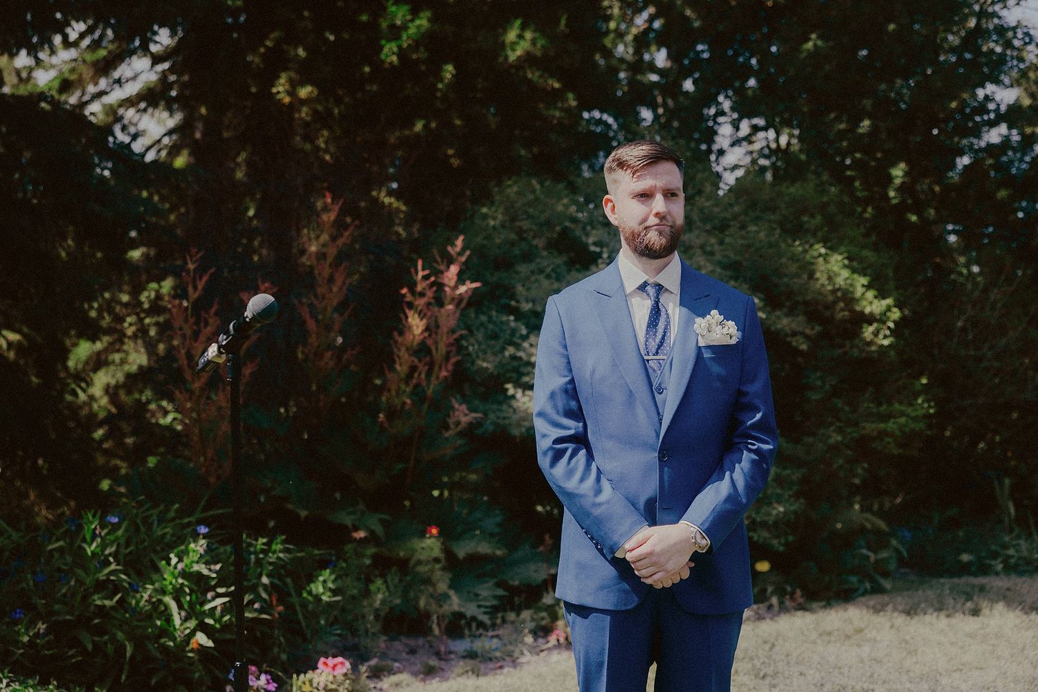 Wedding party members in blue suits standing outdoors among trees.