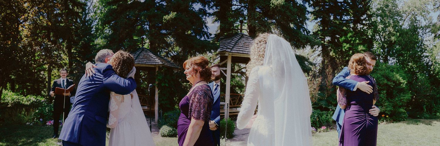 Wedding party shares emotional group hug outdoors during celebration.