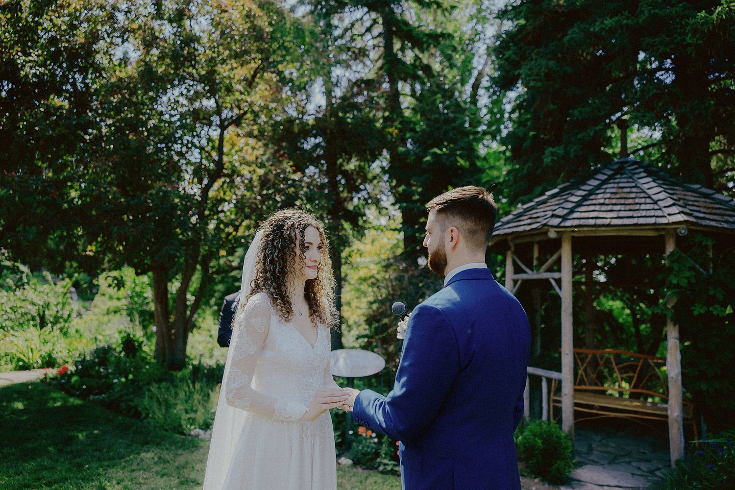 A romantic wedding ceremony takes place in a garden gazebo surrounded by lush greenery.