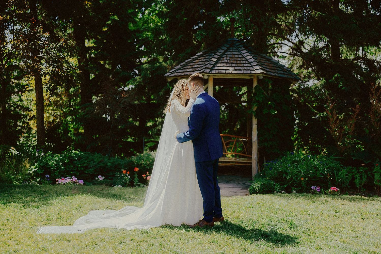 Couple shares romantic moment under garden gazebo during wedding ceremony.