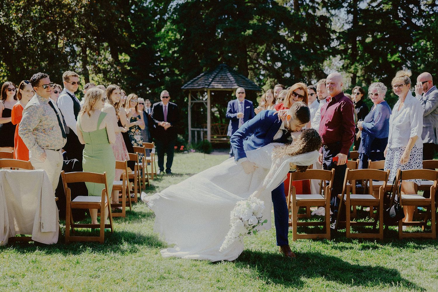 Garden wedding ceremony with wooden chairs and guests in attendance.