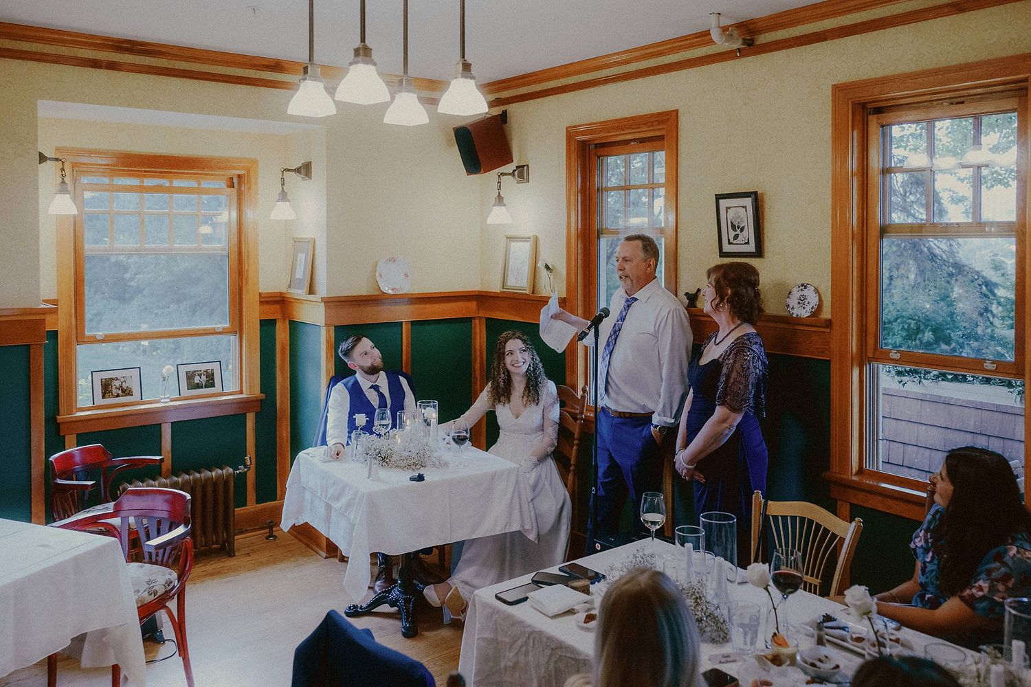 Vintage-style restaurant interior with wood trim and pendant lights during a casual gathering of people at round tables.