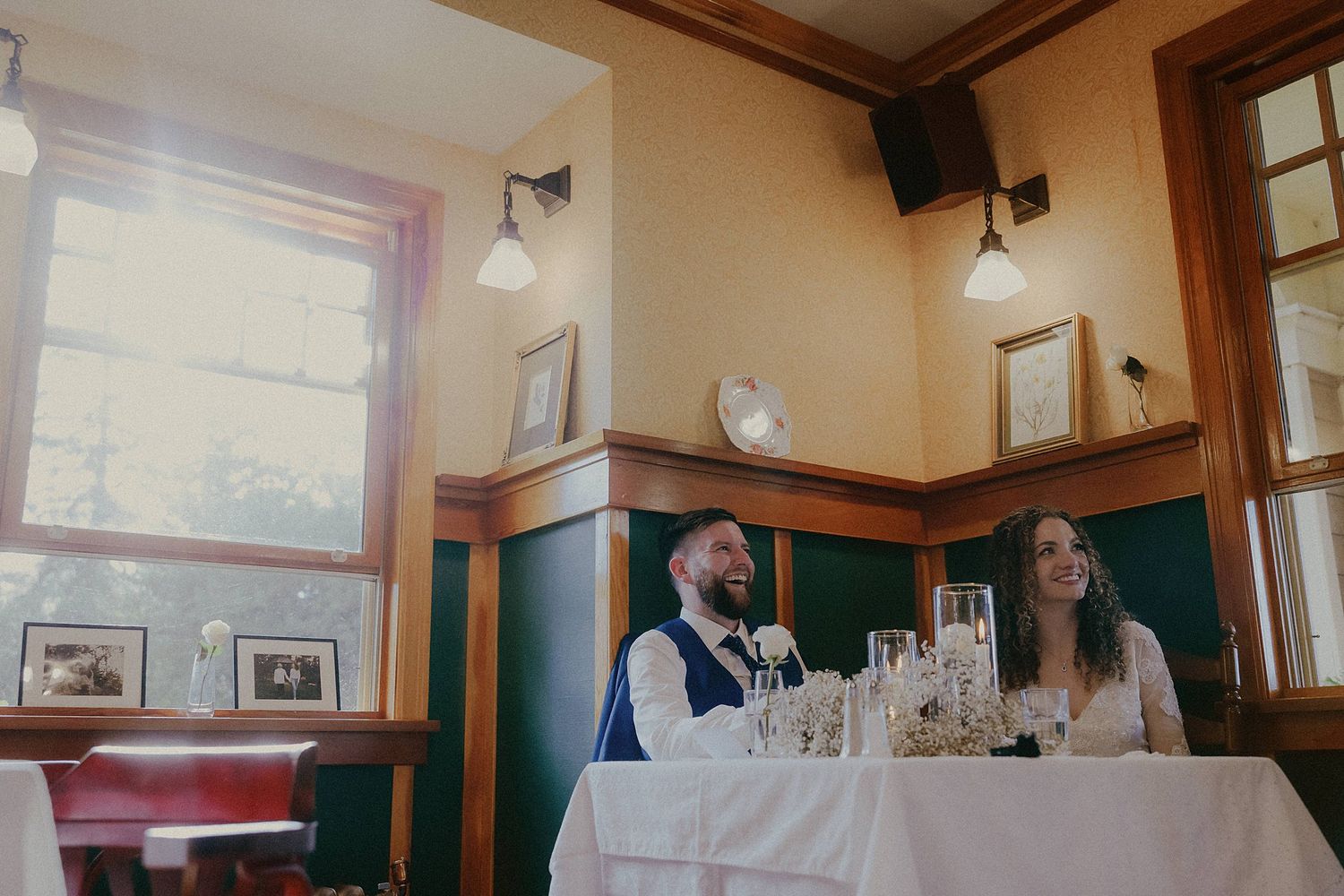 A wedding couple shares a tender moment in a rustic restaurant dining room with wooden panels and vintage decor.
