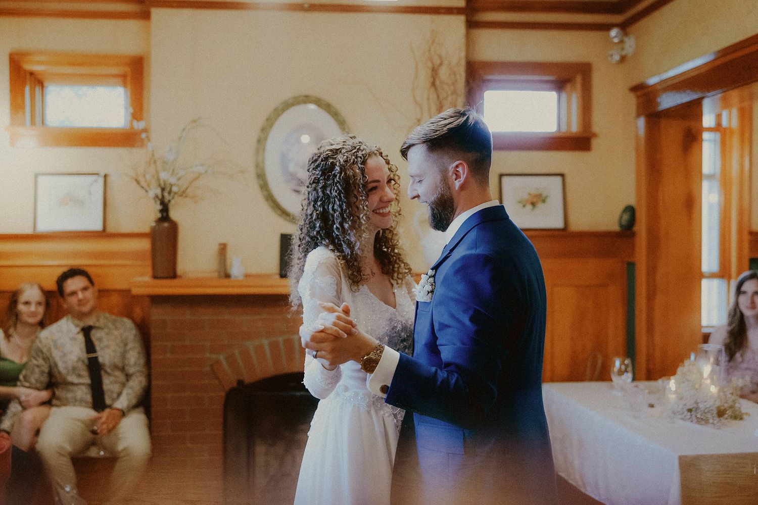 A tender wedding dance moment in a cozy wood-paneled room with natural light.