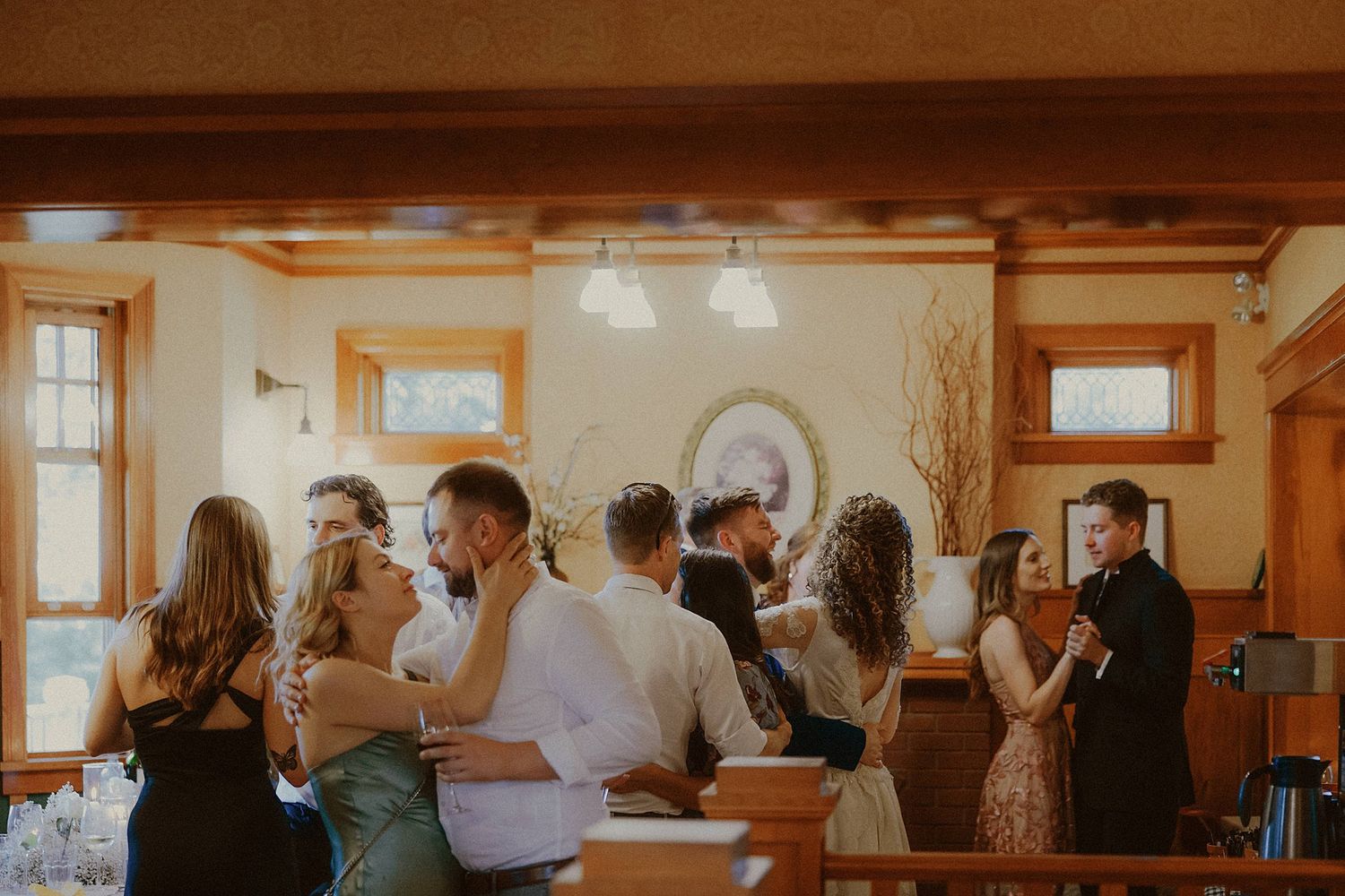 A warm-lit indoor gathering of people socializing and mingling in a rustic room with wooden trim and natural lighting.