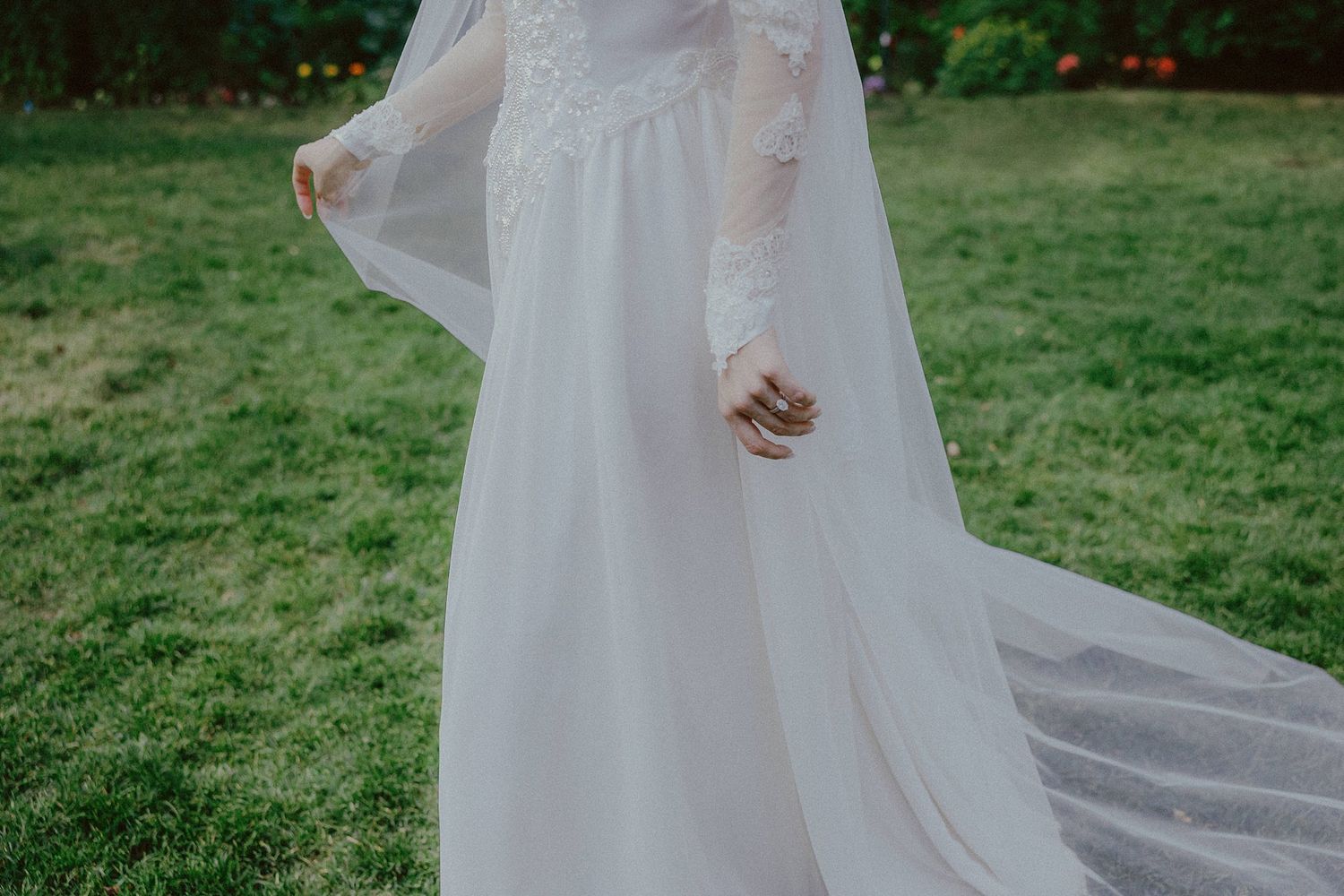 Elegant white wedding gown with flowing train captured in outdoor garden setting.