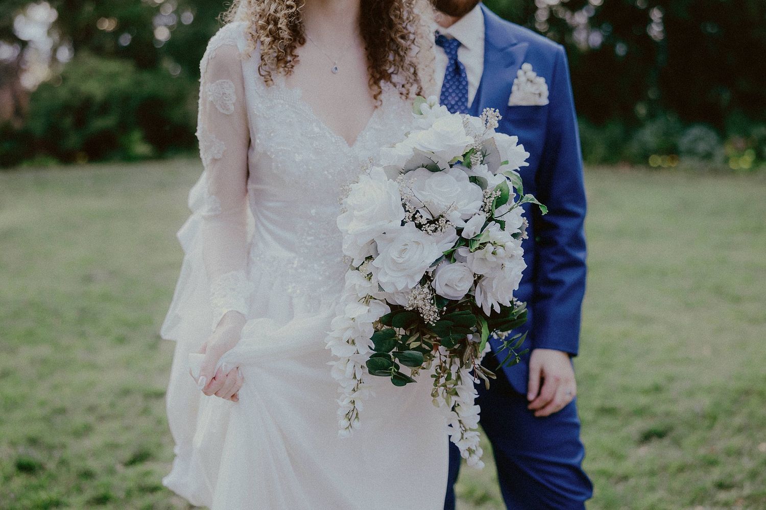 Wedding couple photographed in a lush green garden setting with white floral bouquet.