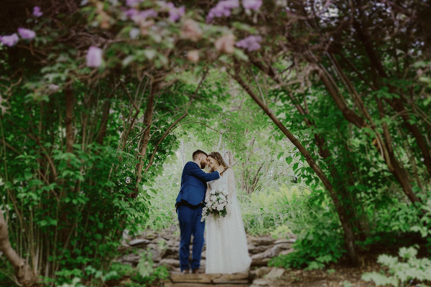 Wedding couple shares intimate moments in a garden setting with blooming flowers.