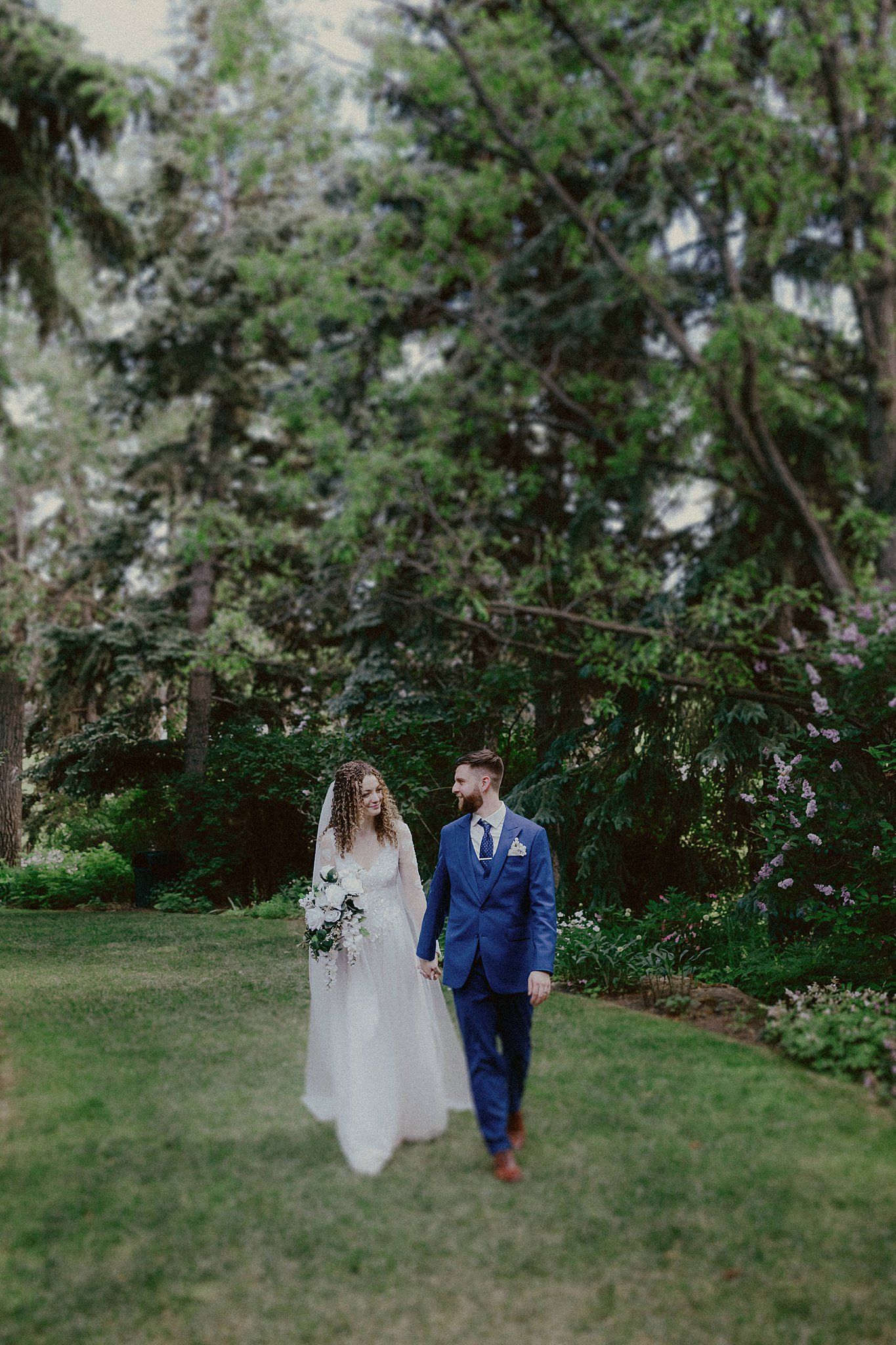 Couple walking together on green lawn surrounded by tall trees and natural scenery.
