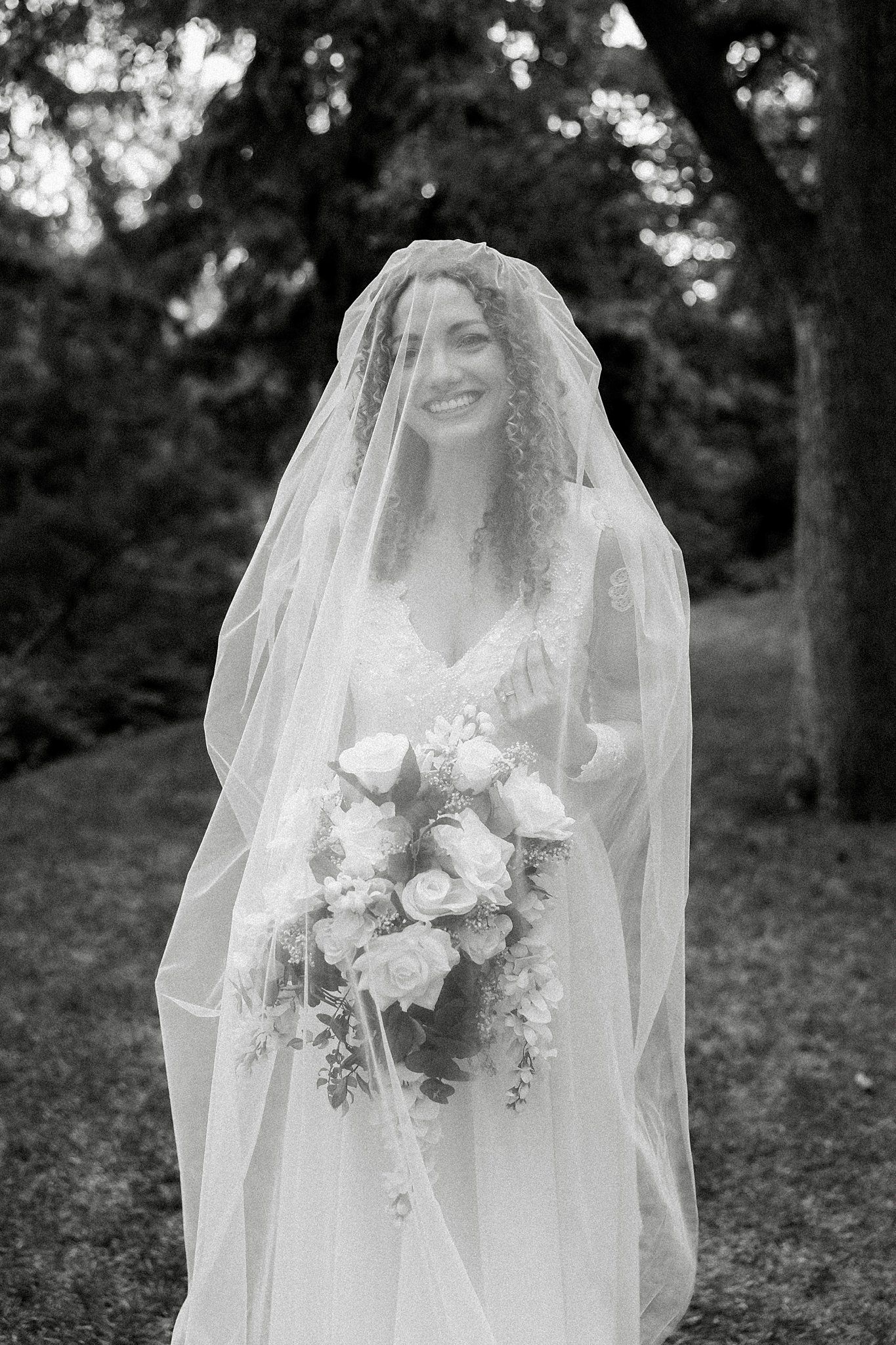 Black and white bridal portraits showing a delicate veil and white floral bouquet in a forest setting.