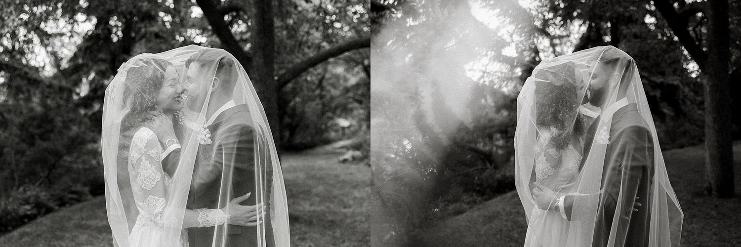 Artistic black and white wedding photography with flowing veil in natural outdoor setting.
