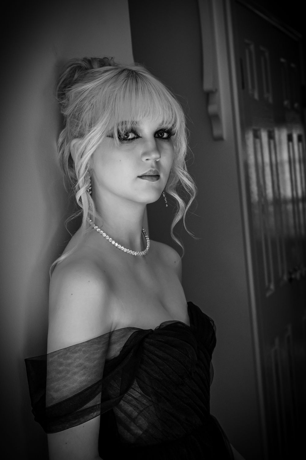 Dramatic black and white photo of a blonde wearing a strapless black dress and pearl necklace.