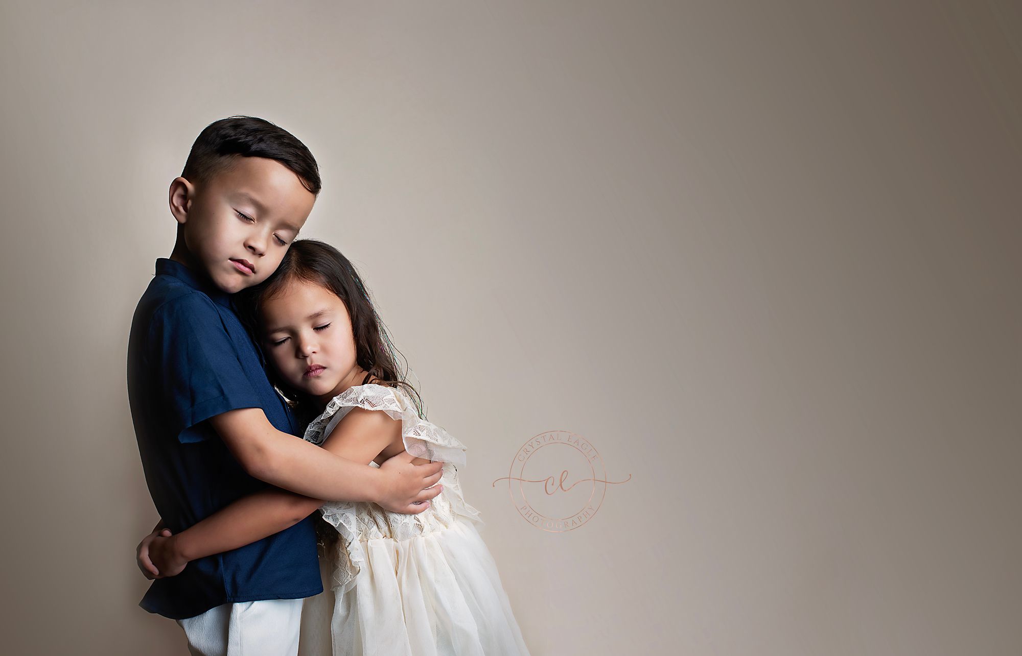 Two young siblings sharing a tender embrace against a neutral background.