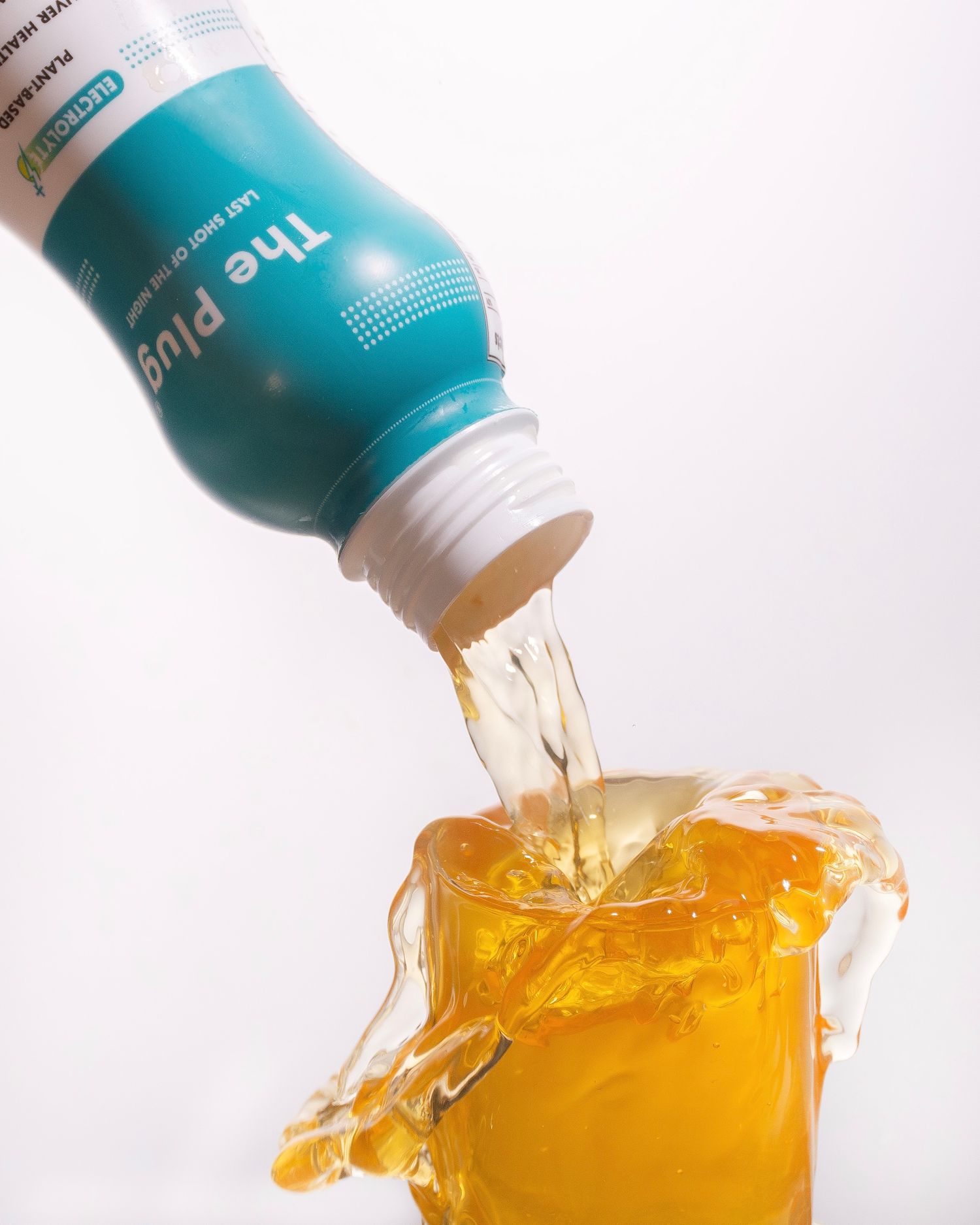 The Plug teal wellness shot bottle pouring golden liquid into an overflowing glass on white background.