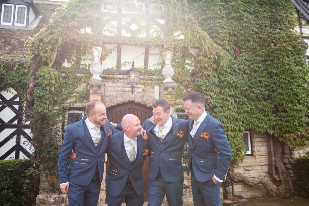 A group of people wearing navy blue suits stand together laughing and smiling outside a stone building.