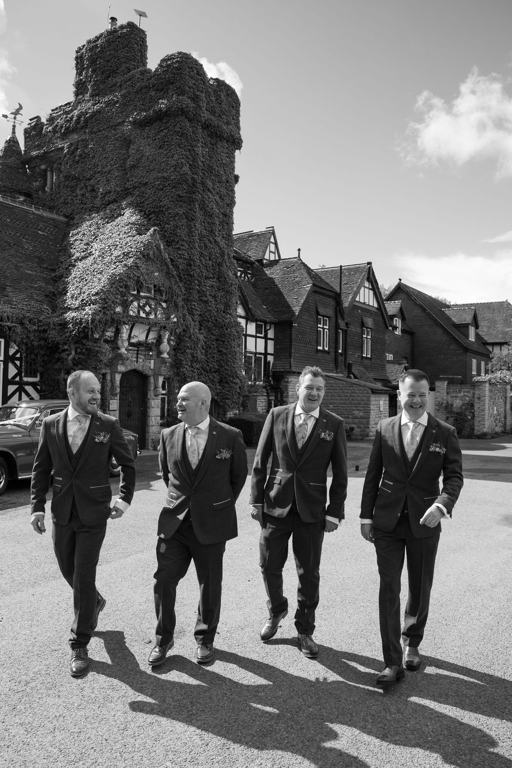 Groomsmen in dark suits walking together on a sunny day casting long shadows.