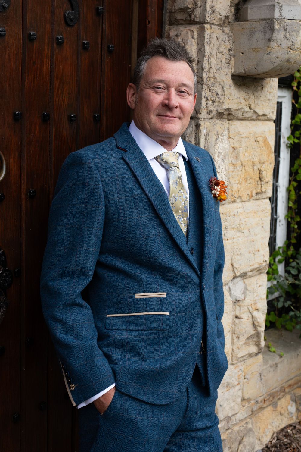 Person in navy blue suit with yellow tie poses against stone wall backdrop.