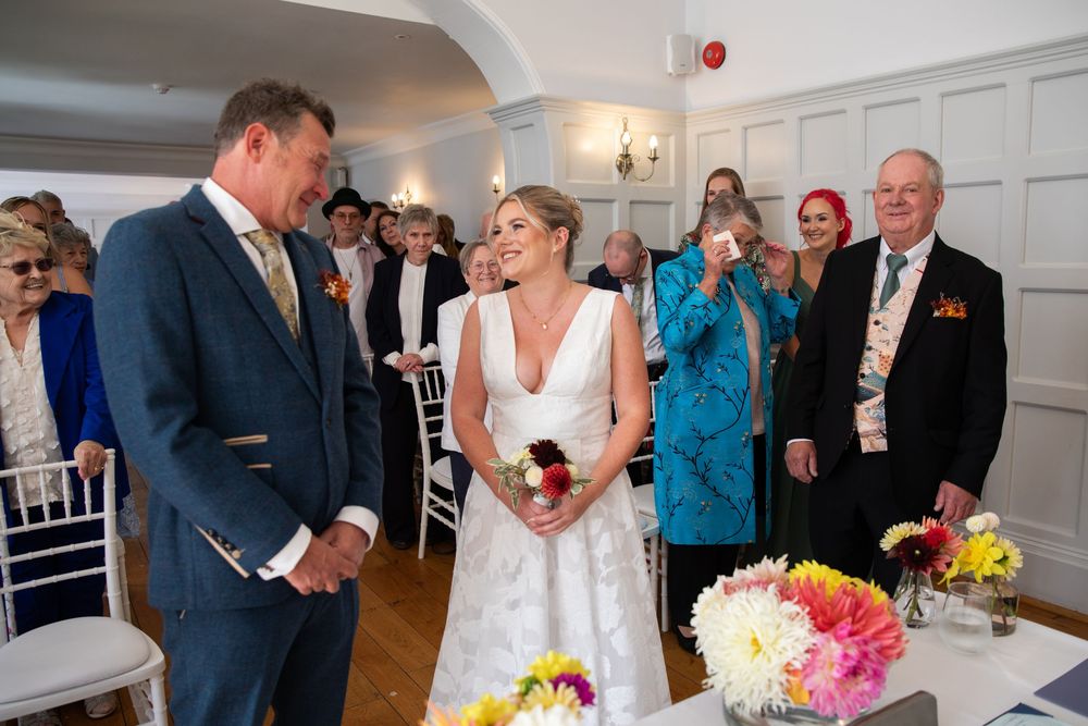 Wedding guests enjoy a lively celebration in an elegant white-paneled room with colorful floral centerpieces.