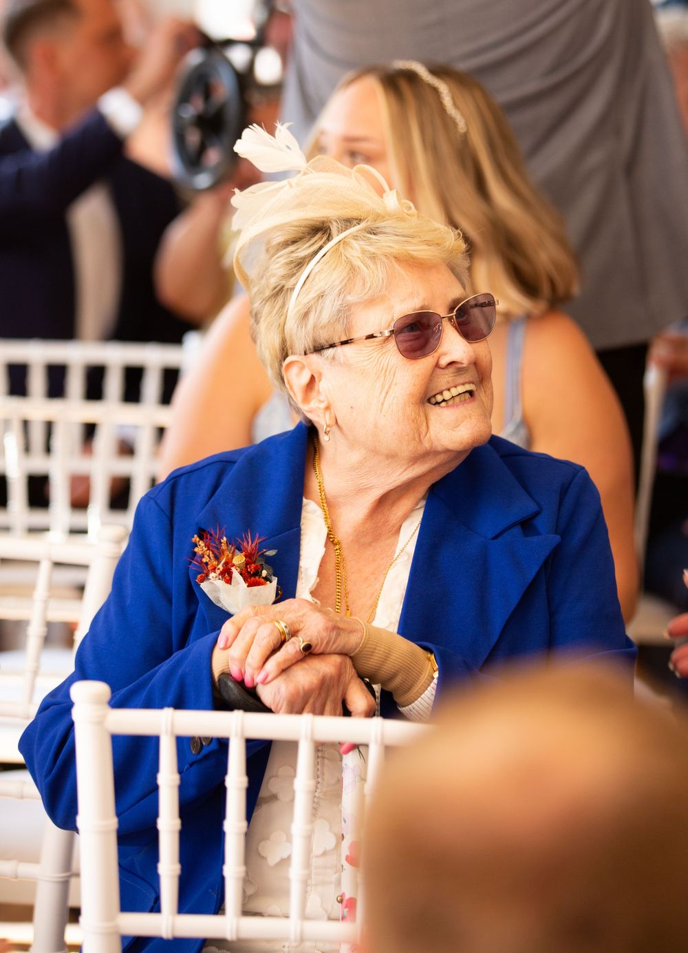 Wedding guest in bright blue blazer sitting at reception table with joyful expression.