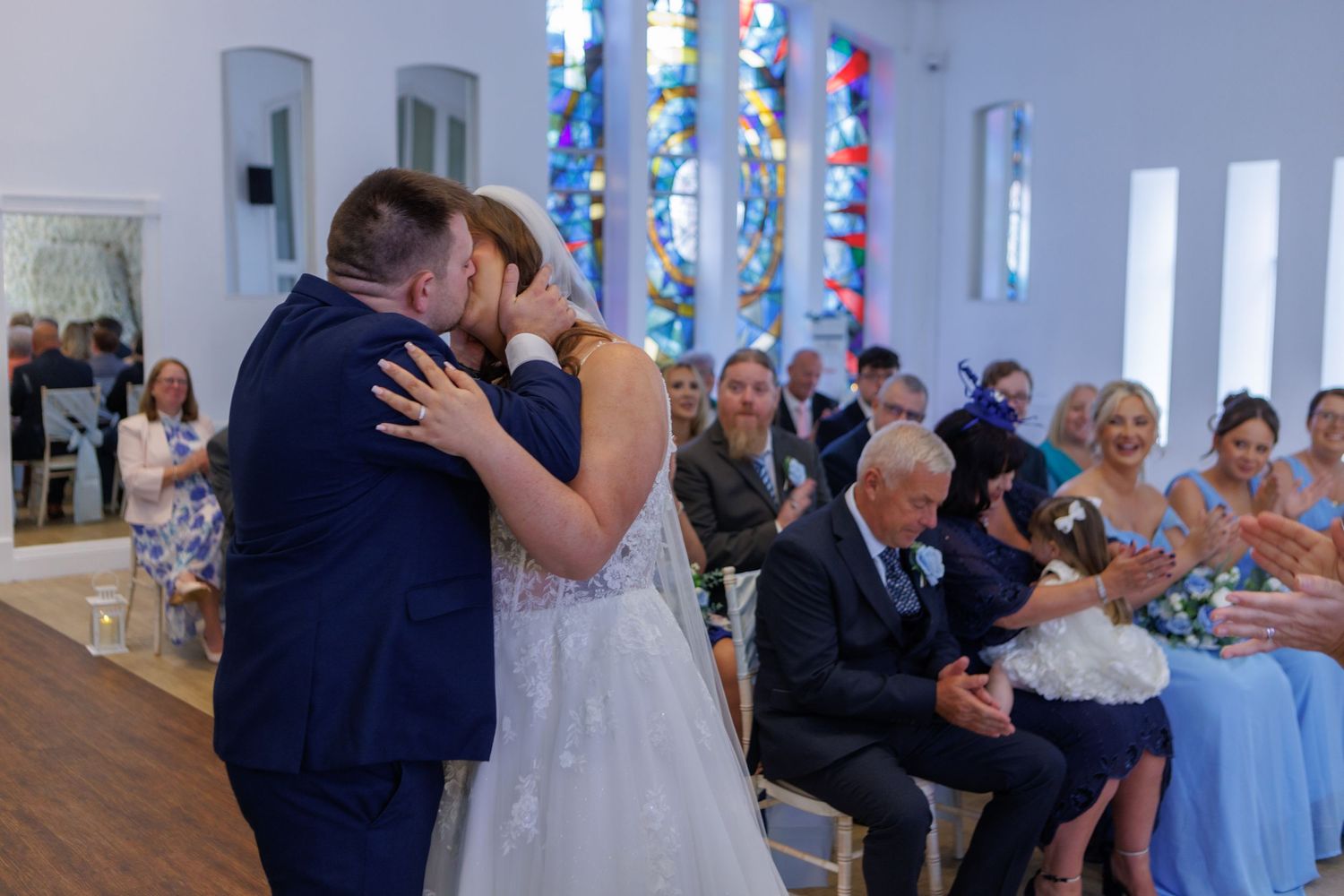 A romantic first dance moment at a wedding ceremony with guests watching in a church with stained glass windows.