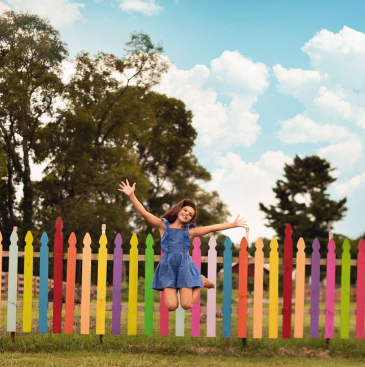 A panoramic sequence shows a joyful person in blue jumping and playing against a scenic natural backdrop with colorful fencing.