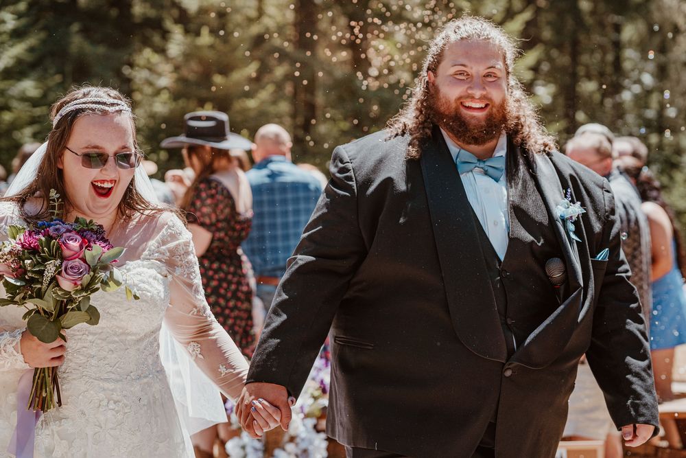 Joyful bride and groom laugh as confetti falls during their outdoor forest wedding celebration.