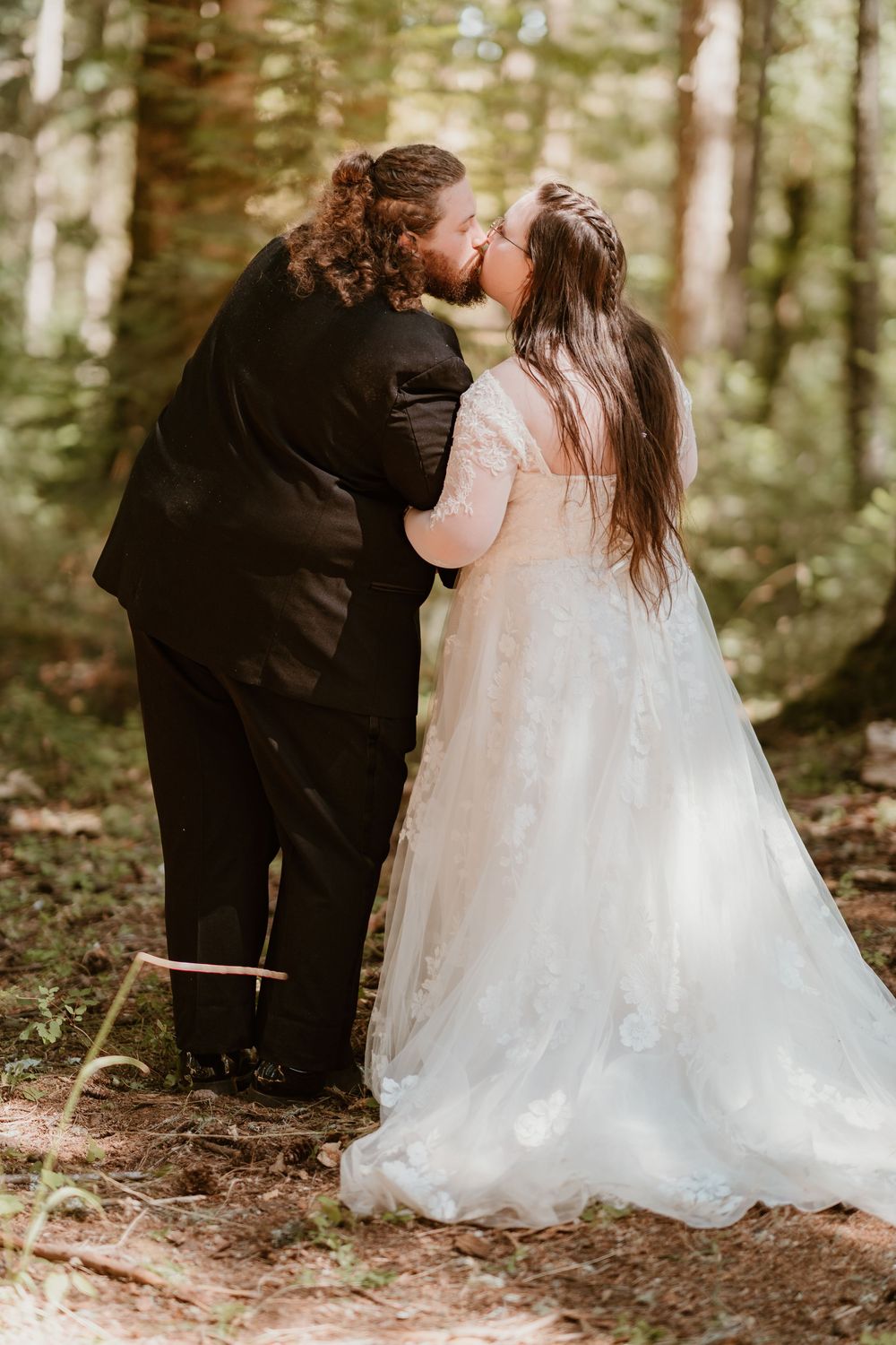 Bride and groom share a romantic kiss in a lush green forest during their wedding day.