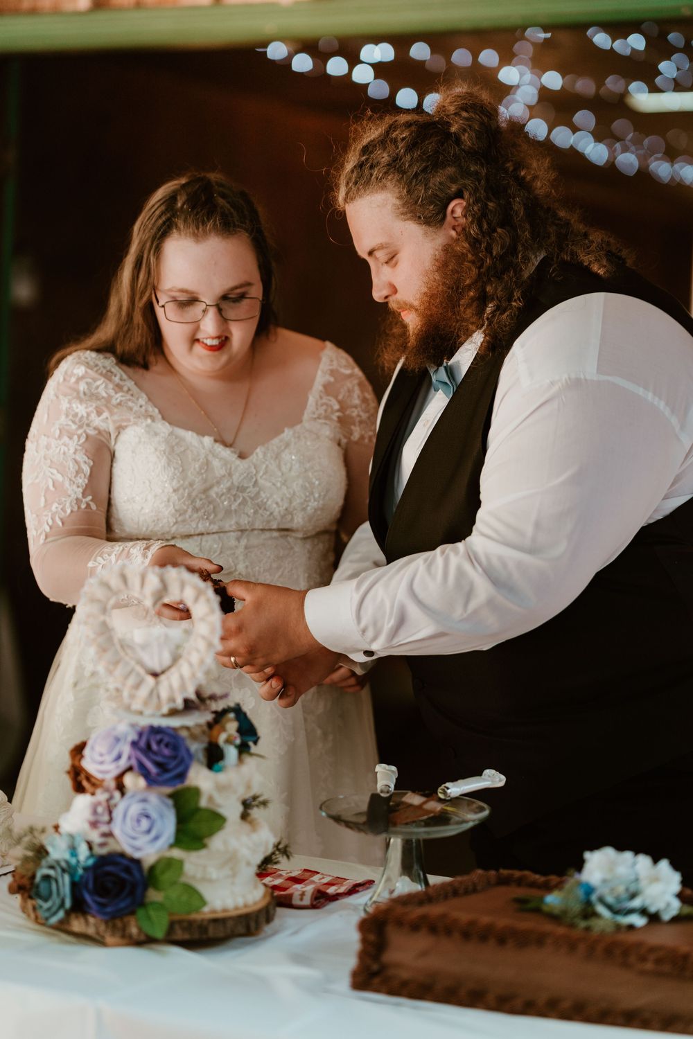 Bride and groom cut their elegant white wedding cake decorated with blue and purple flowers.