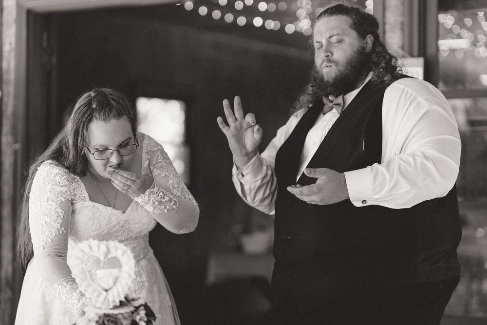 Emotional black and white photo of bride wiping tears as groom gestures during wedding reception.