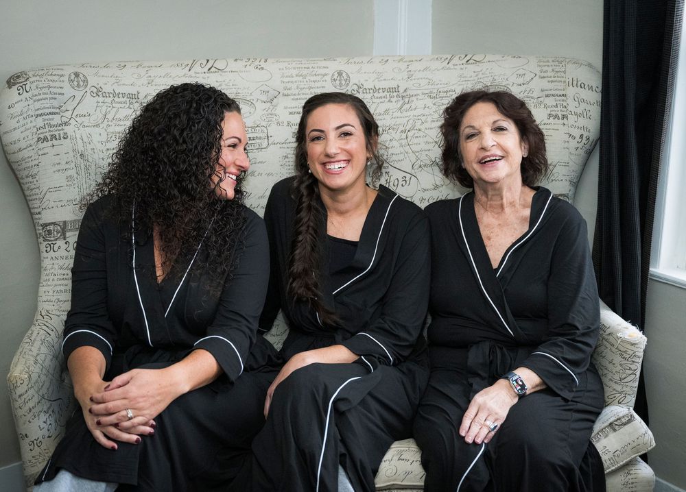 A group wearing matching black outfits sits together on a couch against a white brick wall.
