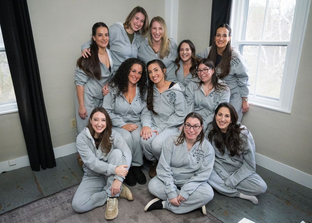 A group wearing matching gray loungewear sits together on the floor in a bright room.