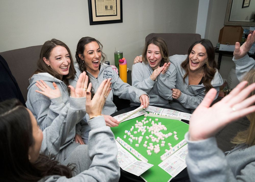 Bridesmaids in matching gray robes gathered around a table playing a wedding day game.