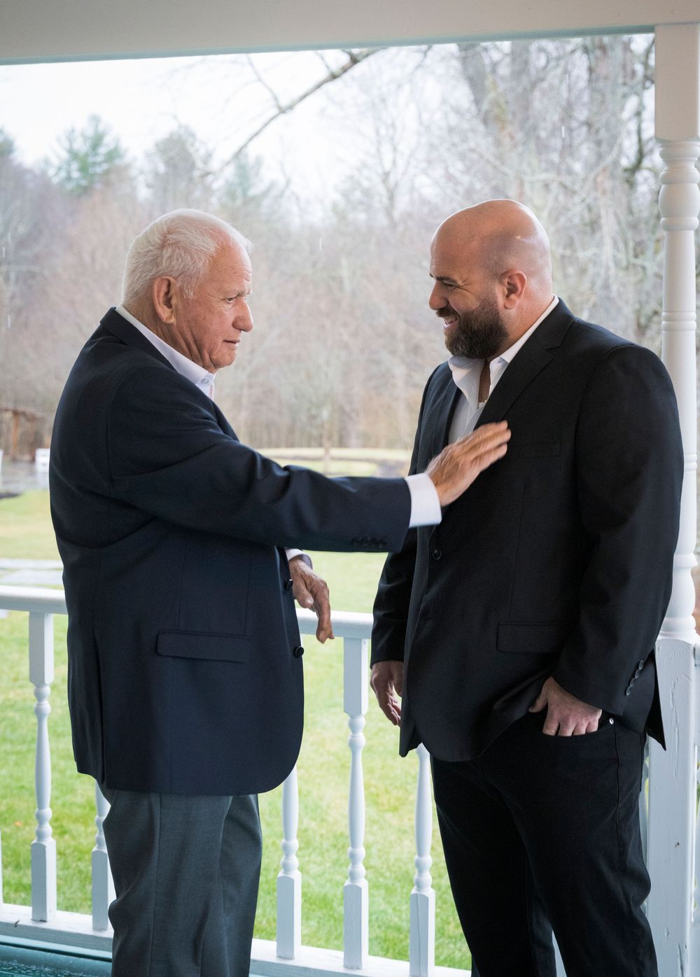 A series of emotional first look photos on a porch with men in black suits.