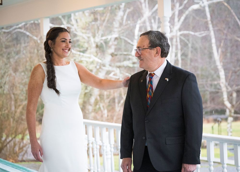 A wedding couple shares intimate moments on a porch with winter trees in the background.